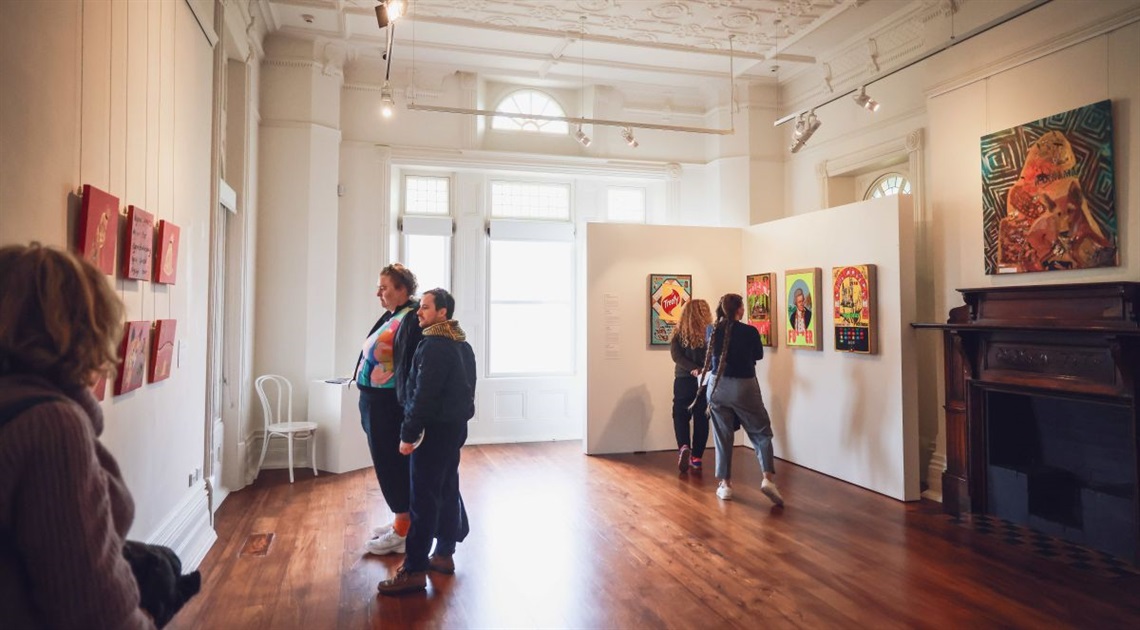A group of people view a collection of artworks hung on a wall