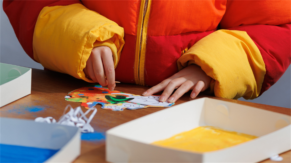 Two hands work on a colourful art project