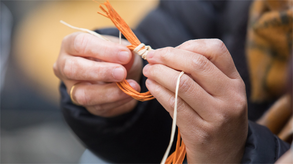 Two hands work on a weaving