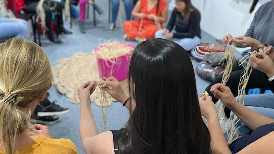 A group of people gather in a circle working on weaving projects