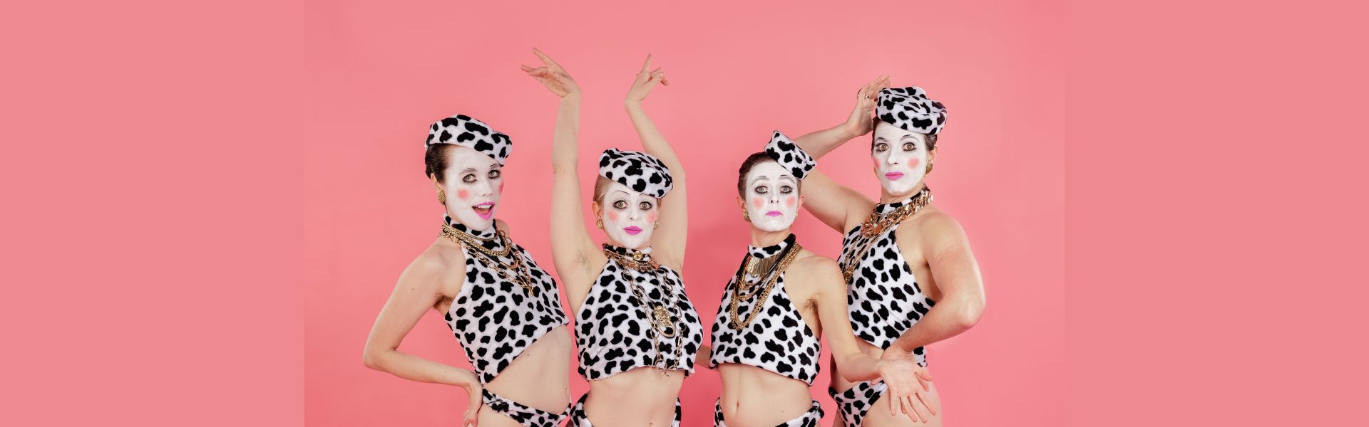 Four people wear cow pattern hats and tanks tops with gold necklaces and clown make up on their faces.