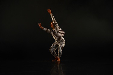 A group of people in grey and white outfits pose across a lit dark stage.