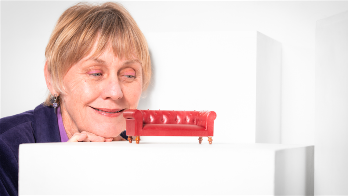 A person peers at a miniature red couch set on top of a white platform.