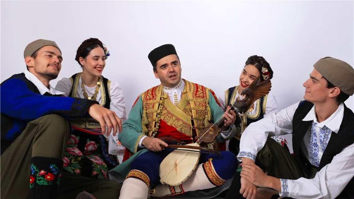 A group of traditional Eastern European musicians sit in a cluster on the the ground.