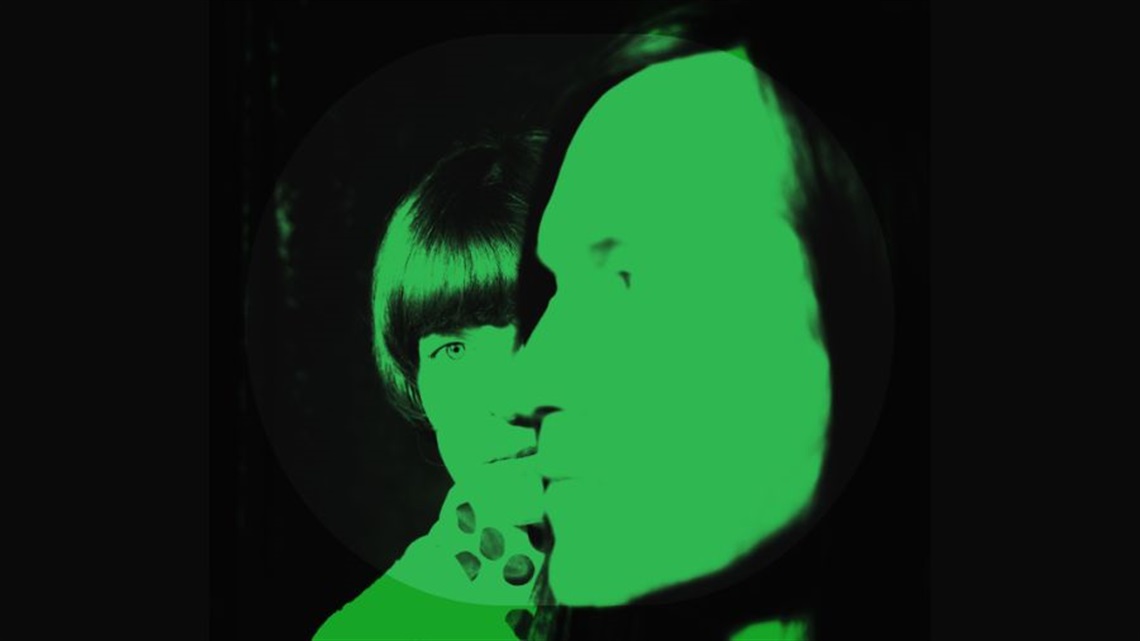 A man in profile, facing left, is in front of a woman with dark hair fringe, facing straight to the camera. A green hue is over their faces.